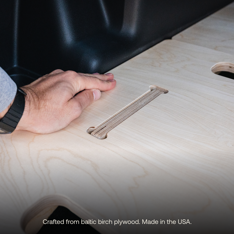 A close-up of a hand touching a smooth, light-colored plywood surface with a handle cutout. The image showcases the texture and grain of the wood. Text at the bottom reads: "Crafted from Baltic birch plywood. Made in the USA by BamBeds." Ideal for your custom Toyota 4Runner Vehicle Sleeping Platform.