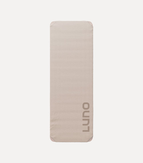 A rectangular, light beige inflatable sleeping pad with rounded corners and the brand name "Luno" printed vertically in gray on one side. It is shown against a plain, white background.