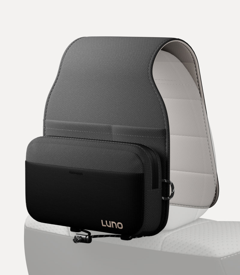A sleek, black travel bag labeled "Luno" is attached to a car seat, shown against a light background. The bag appears to be securely fastened around the headrest area of the seat, which is upholstered in light-colored material.