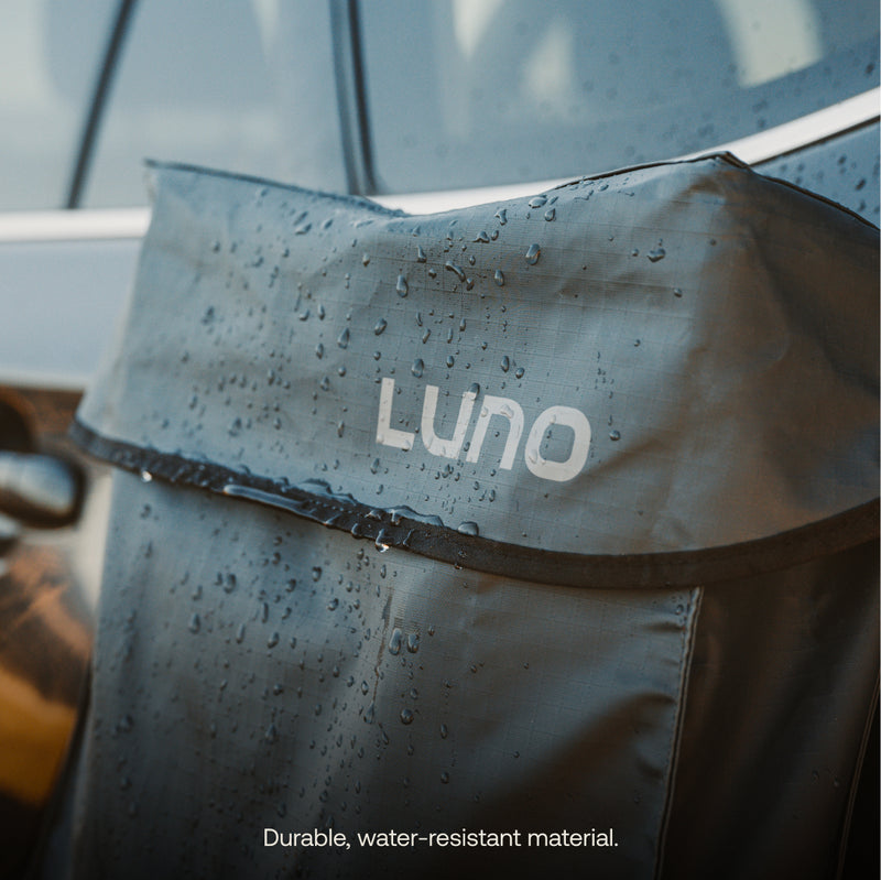 Close-up of a black Luno® Gear & Shoe Storage Bag with water droplets on its surface, attached to a car. Text at the bottom reads “Durable, water-resistant material.”.