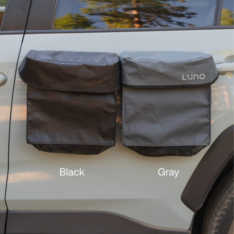 Two rectangular Luno® Gear & Shoe Storage Bags, one black (left) and one gray (right), are attached to the side of a vehicle. Both feature mesh pockets at the bottom for added storage.