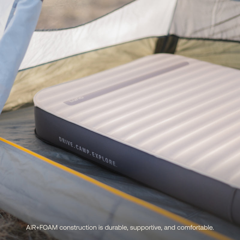 A lightweight, inflatable AIR+FOAM PRO Camping Mattress by Luno® with the text "DRIVE. CAMP. EXPLORE." on its side is set up inside a tent. The close-up shot shows the AIR+FOAM PRO Camping Mattress on the tent floor, highlighting its cushioned texture and inviting appearance. Text at the bottom reads, "AIR+FOAM PRO construction is durable, supportive, and comfortable.