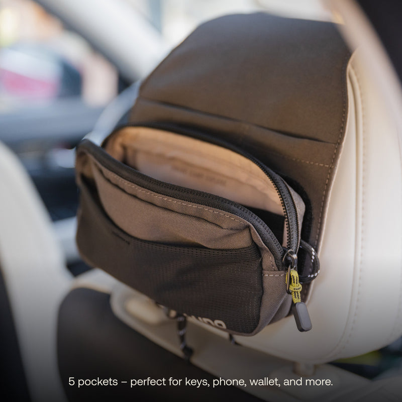 A Luno HQ Headrest Organizer (Pre-Owned) featuring multiple zipped pockets is affixed to the back of a car seat. The user-friendly organizer is slightly open, showcasing its compartments. A caption states, "5 pockets – ideal for keeping keys, phone, wallet, and more neatly organized.