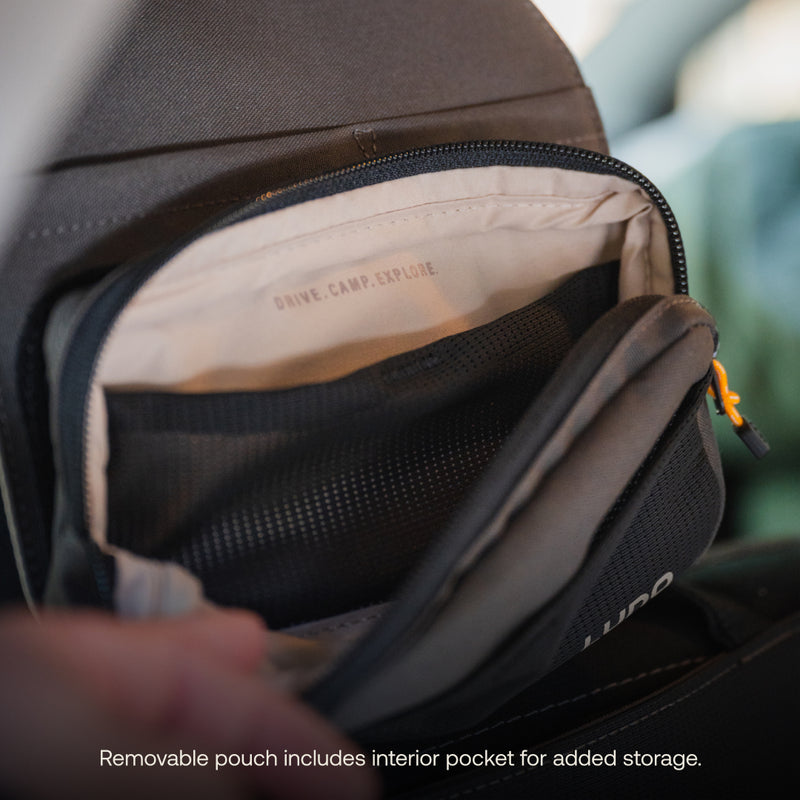 A detailed view of the Luno HQ Headrest Organizer (Pre-Owned) showcases a black removable pouch with an interior pocket, perfect for keeping essentials organized. The flap features the text "DIVE. CAMP. EXPLORE." Additional text notes: "Removable pouch includes interior pocket for added storage." It's ideal as both a headrest organizer and travel companion.