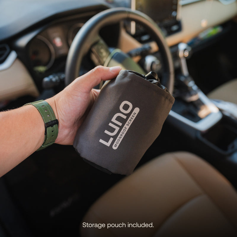 A person holds a black storage pouch featuring the white Luno HQ logo inside a car with a beige interior and visible gear shift. The sunroof window screen from Luno HQ ensures perfect airflow, and at the bottom, it says "Storage pouch included.