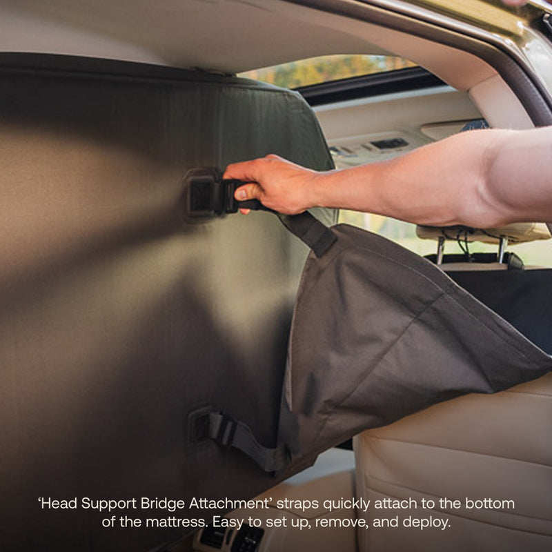 A person secures a strap in a car, attaching a fabric cover to the seat back. Text says it’s the AIR+FOAM Pro Car Camping Mattress’s Head Support Bridge Attachment, made for quick and easy setup and removal.