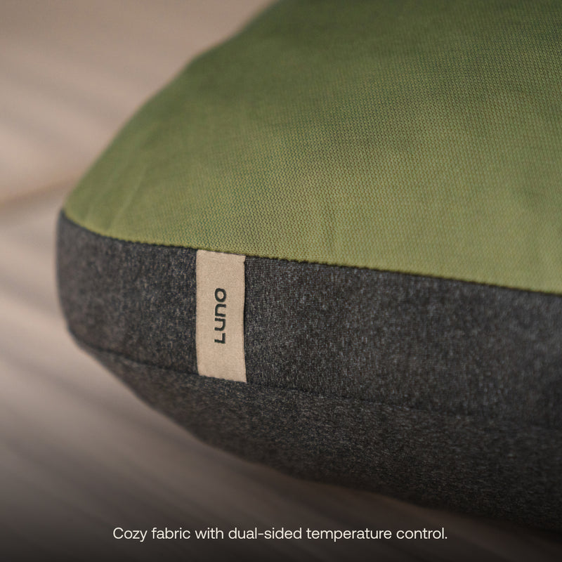 Close-up of a pillowcase with a cozy green and gray polyester blend fabric, sporting a small tag labeled "Luno® Camping Pillowcase." The caption reads, "Ultimate comfort with dual-sided temperature control and cooling moisture-wicking jersey knit.