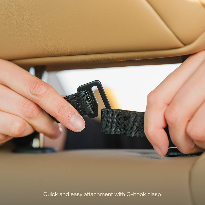 Close-up of hands attaching a black strap with a G-hook clasp to a tan car seat headrest from the Luno HQ Seatback Organizer (Pre-Owned). Text reads: "Quick and easy attachment with G-hook clasp." Enjoy convenient USA shipping on this essential accessory.