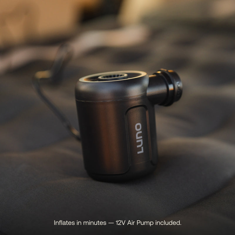 A black Luno® portable air pump with a cord is on a dark textured surface, ideal for inflating your AIR Pro Vehicle Mattress in minutes—12V Air Pump included. Text below: "Inflates in minutes.