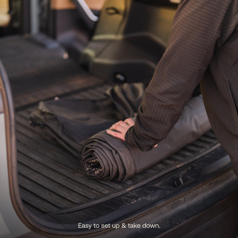 In the back of a vehicle, someone rolls out the dark Luno® AIR Pro Vehicle Mattress. Text reads, "Easy to set up & take down.
