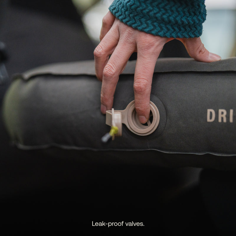 A hand in a teal sleeve delicately adjusts the valve on a dark air surface marked "DRI," ensuring a perfect fit for the Luno® AIR Pro Vehicle Mattress. Caption: "Leak-proof valves.