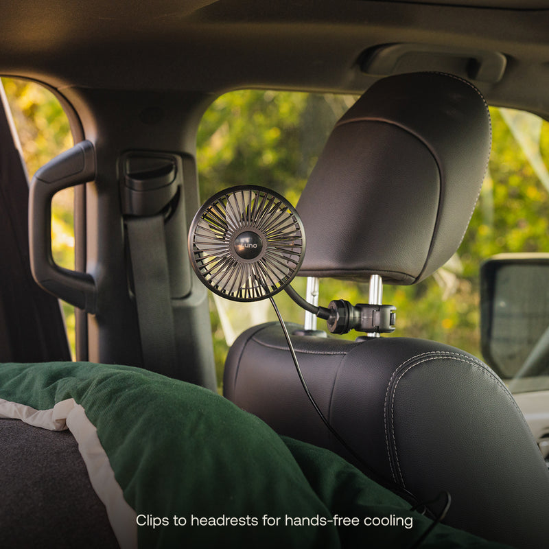 A compact black Luno® Camping Fan, powered by USB-C, clips to a car’s headrest to provide hands-free cooling and 360° airflow control for back seat passengers.
