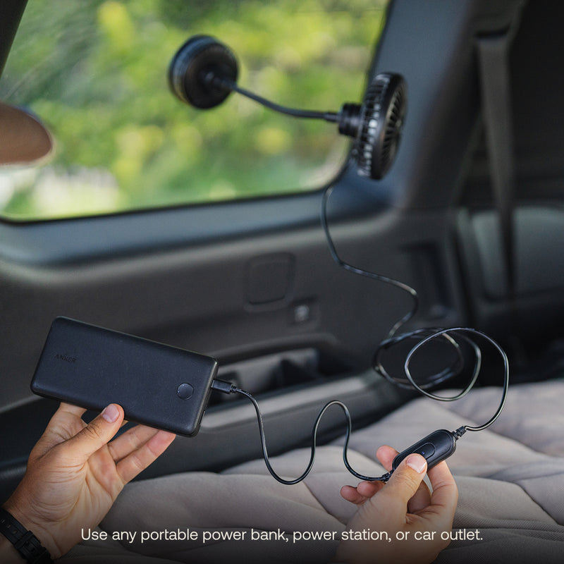 A person plugs a Luno® Camping Fan with 360° airflow control, mounted on a car window, into a black portable power bank. Text reads: "Use any portable power bank, power station, or car outlet." Greenery is visible outside.