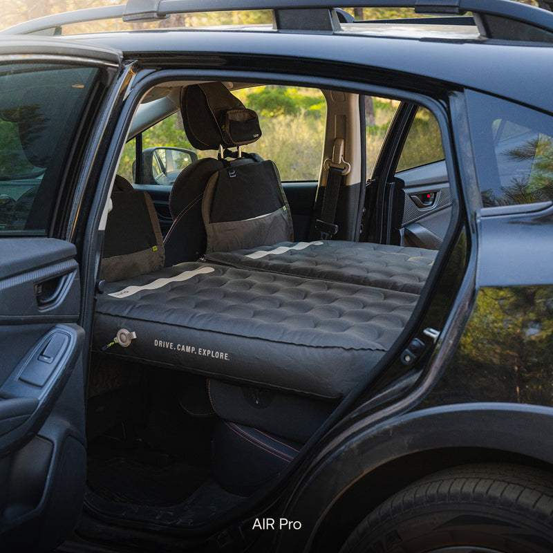 The Subaru Crosstrek Car Camping Mattress is set up across the back seat, creating a flat, comfortable sleeping space—ideal for adventure-ready car camping with the doors open in an inviting outdoor scene.