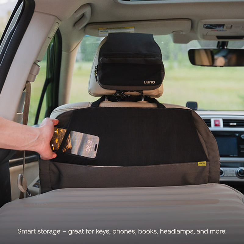 A person puts a smartphone into a black and gray Luno storage organizer on the back of a car seat—ideal for keeping essentials handy during trips with your AIR+FOAM Pro Jeep Wrangler Mattress. Another storage pouch is attached to the headrest.