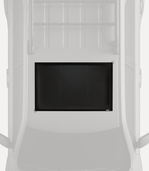 An overhead view of the interior of a vehicle with a minimalist design, showing a rectangular black mesh pet barrier secured between the front seats and the cargo area. The barrier is designed to keep pets safely contained in the back while driving.
