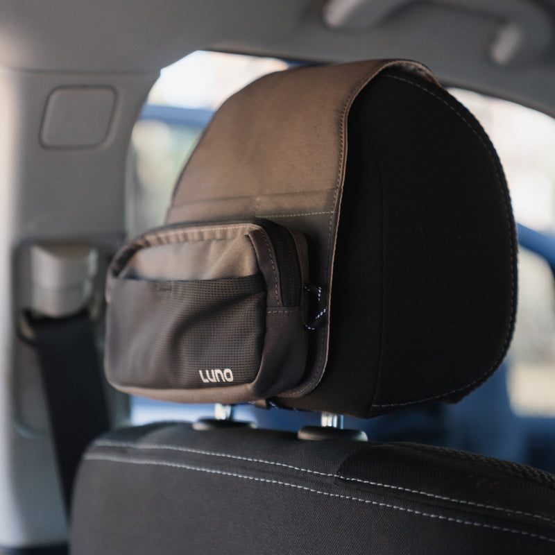 A pre-owned Headrest Organizer from Luno HQ offers practical organization with an easy-to-install design. It features a small zipped compartment and is displayed against a backdrop of a vehicle, showing a partially visible seatbelt and a blurred window.