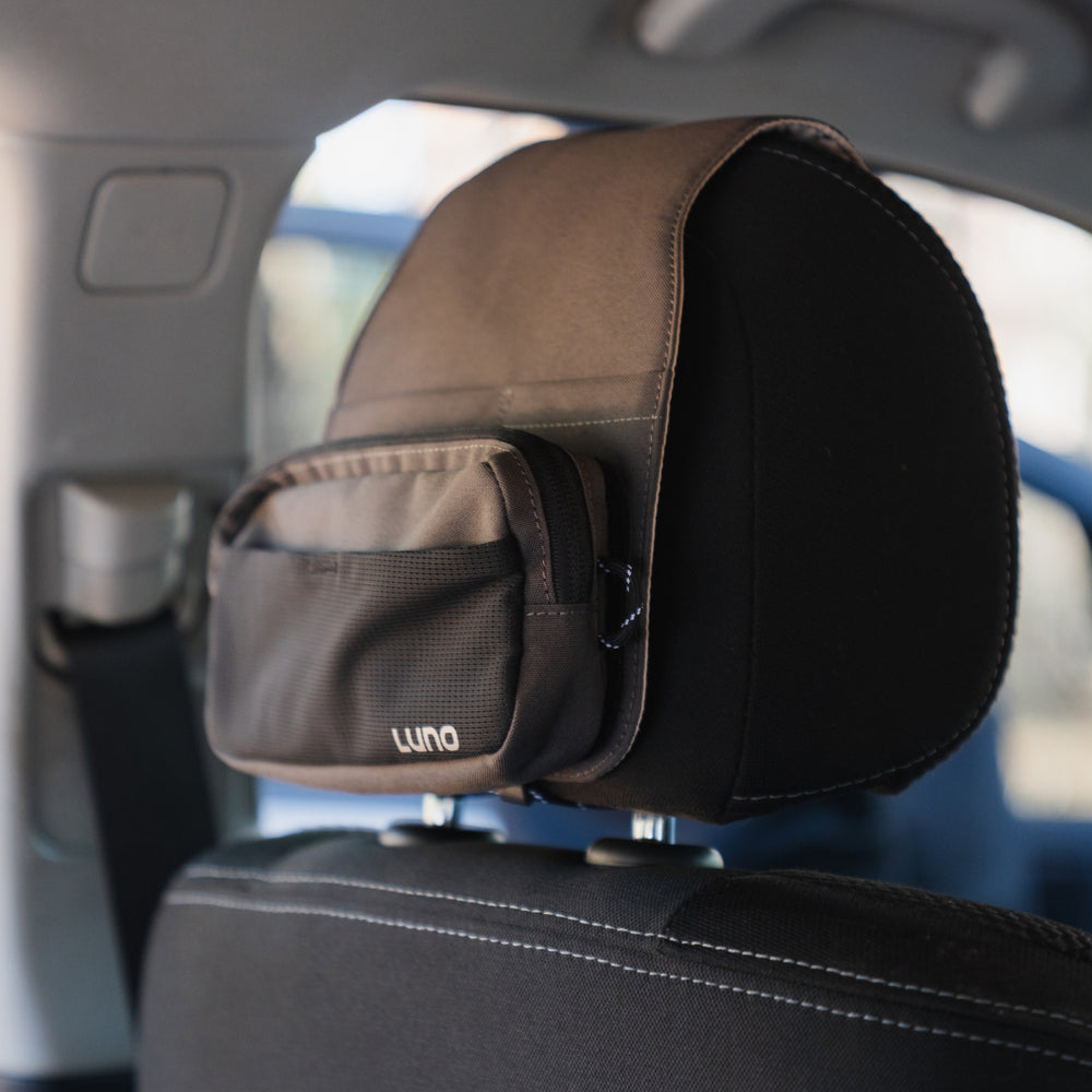 A pre-owned Headrest Organizer from Luno HQ offers practical organization with an easy-to-install design. It features a small zipped compartment and is displayed against a backdrop of a vehicle, showing a partially visible seatbelt and a blurred window.