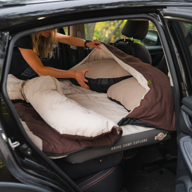 Someone sets up a Luno® Packable Camping Pillow and bedding in their car’s back seat, creating a cozy sleep area with a mattress designed to fit the vehicle’s interior.