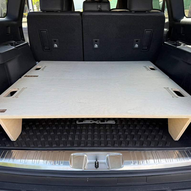 The Vehicle Sleeping Platform with cutout handles is set in the SUV cargo area, providing a raised flat surface for storage or sleeping while the rear seats remain upright in the background.