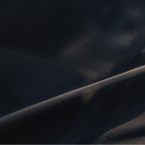Close-up image of a dark, textured fabric, illuminated by subtle lighting that creates soft highlights and shadows, showcasing the material's detailed weave and smooth surface.