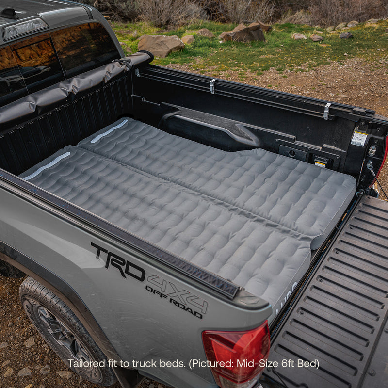 A Luno® AIR Truck Bed Mattress in gray, designed for a gray TRD 4x4 Off Road with a mid-size 6ft bed, is shown fully laid out on the lowered tailgate, offering a comfortable sleeping area.