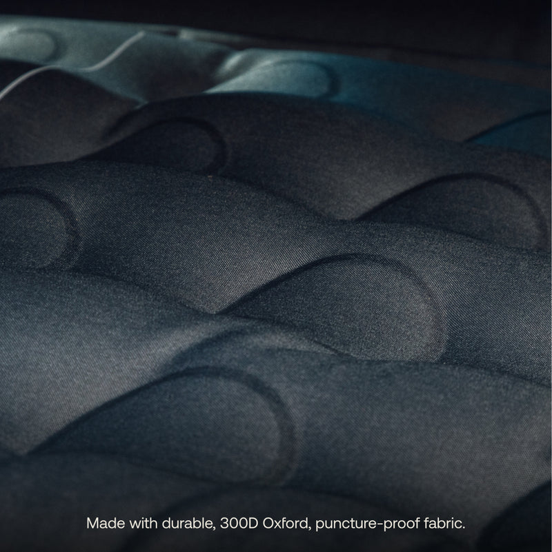 Close-up of a dark-colored Luno® AIR Truck Bed Mattress featuring raised, wavy textures. Text at the bottom: “Made with durable, 300D Oxford puncture-proof fabric for a comfortable sleeping area.”.