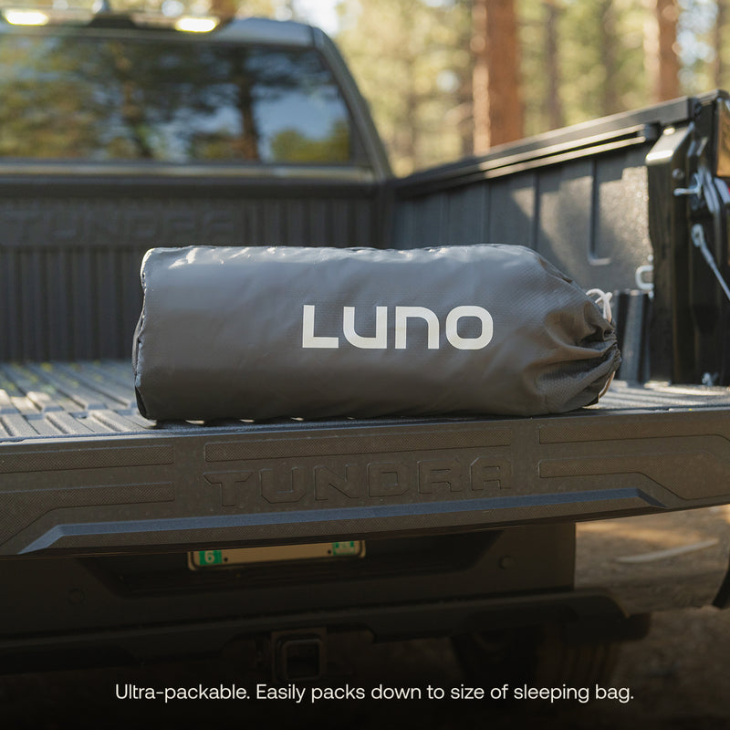 A Luno® bag rests on the bed of a black Toyota Tundra, surrounded by trees. Caption: "Ultra-packable. Pairs perfectly with your Luno® AIR Truck Bed Mattress for a streamlined sleeping setup.