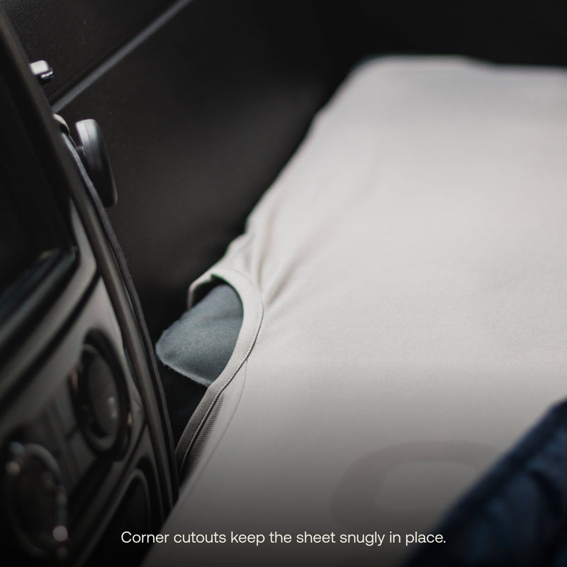 Close-up of the AIR Van Front Cab Mattress Fitted Sheet by Luno HQ, in gray with corner cutouts, snugly covering a car seat. Part of a car's dashboard is visible in the background. In condition marked as pre-owned, text at the bottom reads, "Corner cutouts keep the sheet snugly in place.