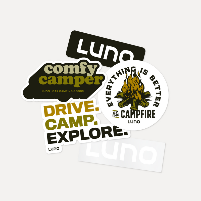 The Camping Sticker Pack by Luno HQ includes vinyl window stickers with phrases like "comfy camper," "DRIVE. CAMP. EXPLORE.," and "EVERYTHING IS BETTER BY THE CAMPFIRE"—perfect for your car camping setup.