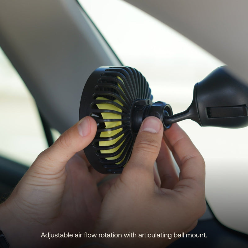 An individual adjusts a pre-owned Luno HQ Camping Fan in like-new condition, which is mounted in a car with an articulating ball mount. This fan has black blades accented with green and is positioned close to the window. Below it reads, "Adjustable airflow rotation with articulating ball mount." USA shipping available.