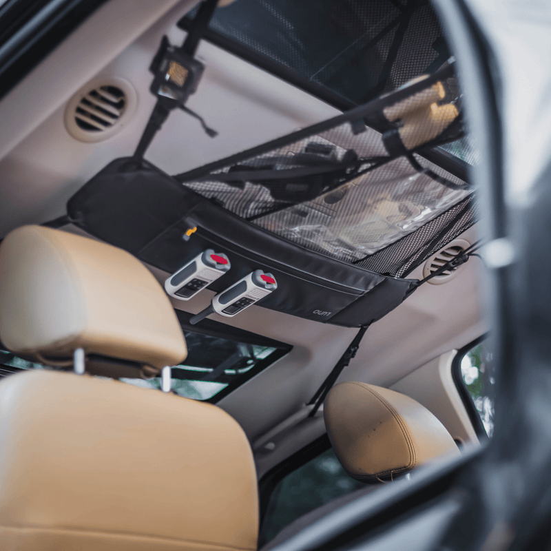 Snapshot from within a car highlights a clever storage solution: a pre-owned Cargo Hammock by Luno HQ, in black, affixed to the ceiling. This portable gear shelf, with its mesh pockets, gracefully hangs above the beige leather seats.
