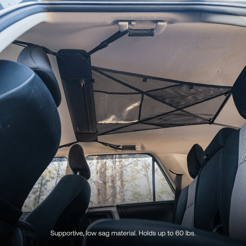 Interior view of a car featuring the Luno HQ Cargo Hammock (Pre-Owned), a smart storage system supporting up to 60 lbs. This net extends across the cabin above the seats, providing a portable gear shelf that is securely anchored to the roof for additional storage space.