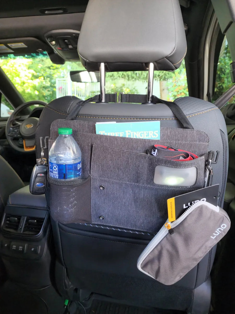 A car seat organizer attached to the back of a front seat. The organizer holds a water bottle, a book titled