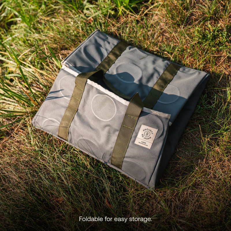 A folded Gear Tote | 50L from Luno HQ with green carry handles lies on grass. It has a tag showcasing the brand logo and appears to be an excellent solution for easy packing. The text at the bottom reads, "Foldable for easy storage.