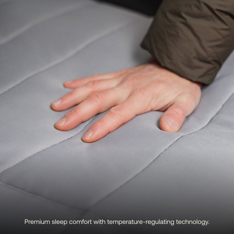 A hand pressing down on a gray mattress topper with a quilted pattern demonstrates its comfort. The text at the bottom reads, "Luno HQ's premium sleep comfort with temperature-regulating technology." Ideal for car camping trips or enhancing your comfy Memory Foam Topper (Pre-Owned).