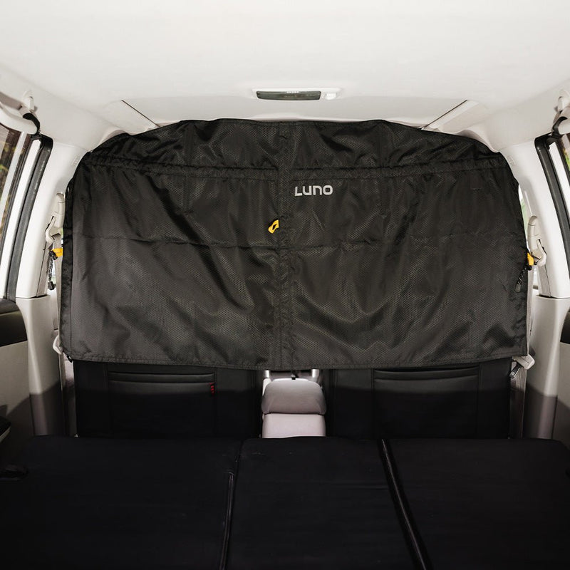 The interior of the vehicle showcases a black "Luno HQ" Car Privacy Curtain (Pre-Owned), installed securely behind the front seats to offer separation from the rear seats. The well-lit image accentuates the curtain's texture and quality, making it an ideal choice for anyone interested in pre-owned gear for enhanced privacy.