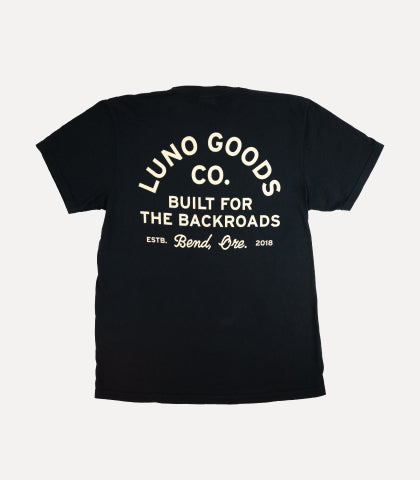 A black t-shirt with white text on the back that reads "Luno Goods Co. Built for the Backroads. Est. Bend, Ore. 2018." The text is arranged in a semi-circular pattern on the upper part of the shirt.