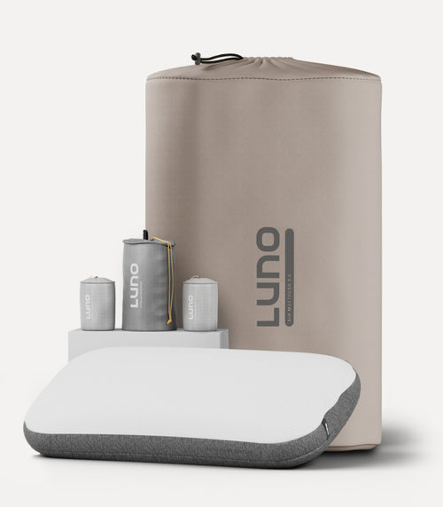 A beige and gray travel pillow set with the brand name "Luno" displayed prominently. The set includes a white and gray pillow, a matching travel bag, and three compact silver cylinders. The items are neatly arranged against a plain background.