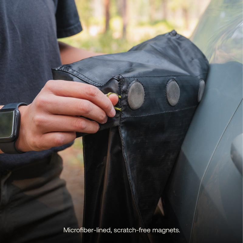 A person attaches the black Luno® Gear & Shoe Storage Bag, lined with microfiber and featuring scratch-free magnets, to the side of a car. The text at the bottom reads: "Microfiber-lined, scratch-free magnets.