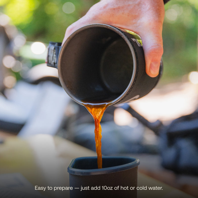 A hand is pouring a dark brown liquid from a black cup into a smaller container. The slightly blurred background suggests an outdoor setting, perfect for adventures. At the bottom of the image, there's a caption that reads: "Campers Blend Instant Craft Coffee by Luno® — Easy to prepare — just add 10 oz of hot or cold water.