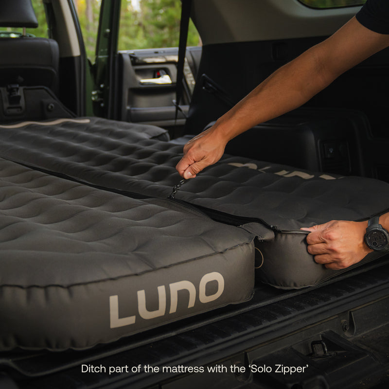 A person unzips a Luno® AIR Pro 4Runner Vehicle Mattress in a car’s back, demonstrating the removable section with its "Solo Zipper." Text below: "Ditch part of the mattress with the 'Solo Zipper'.