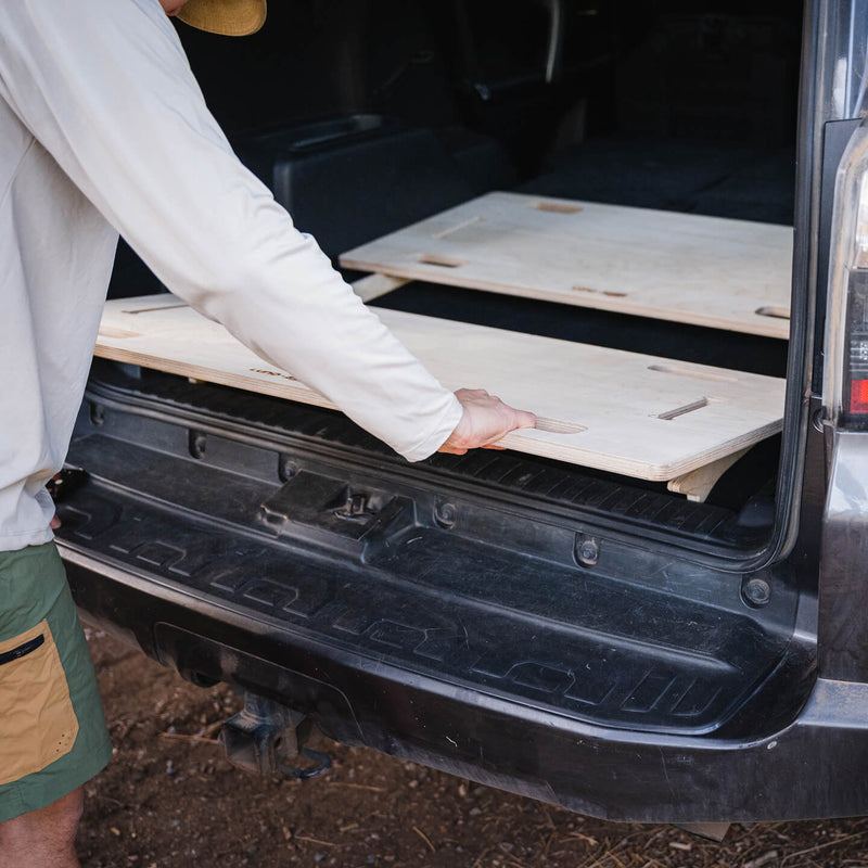 A person installs the Vehicle Sleeping Platform in the back of a car, turning the cargo area into an organized space for storage or comfortable rest during travel.