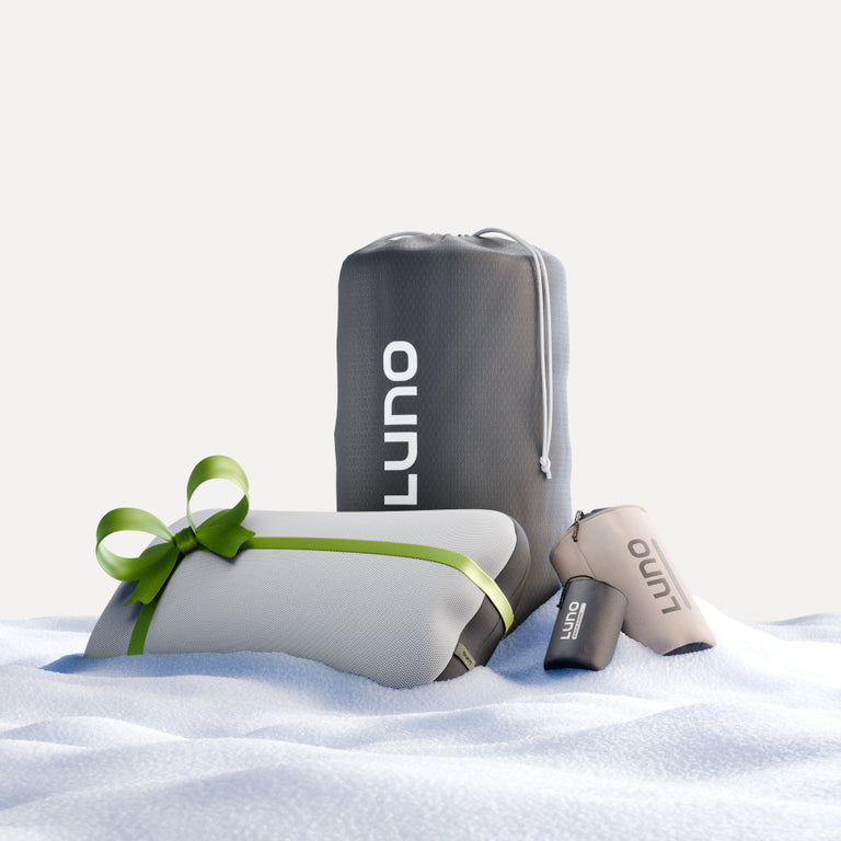 The Camper Van AIR Starter Bundle from Luno® is perfect for creating a minimalist and clean aesthetic in your cozy spare bedroom. This bundle features a rolled sleeping pad tied with a green ribbon, along with a drawstring bag, and two small pouches in beige and gray, all set on a soft, textured surface.