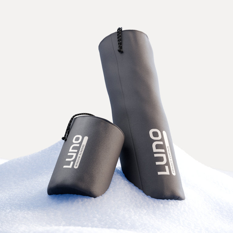 Two black insulated bottle sleeves featuring the Luno® logo are set against a snowy backdrop, perfect for car camping. One stands upright while the other lays flat, both equipped with drawstring closures for secure storage as part of the Car Camping Privacy Bundle.