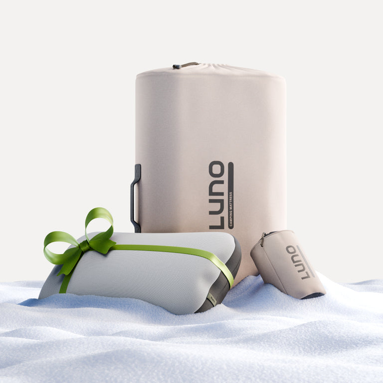 Luno® branded camping items are nestled on a soft, snowy surface, making them ideal for comfortable outdoor adventures. These include a large cylindrical bag, a smaller gift-wrapped pouch with a green ribbon, and a compact travel case—essential companions for car camping or enjoying the 4Runner AIR+FOAM Pro Sleep Bundle.