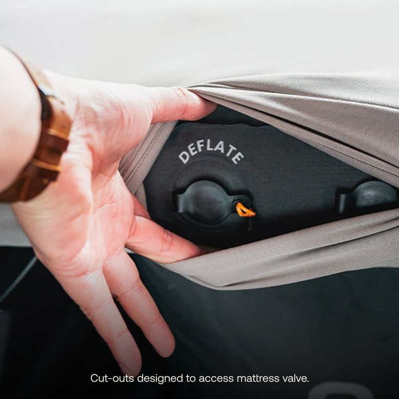 A hand gently pulls back the fabric to reveal a mattress valve labeled "DEFLATE." The text at the bottom reads, "The Luno HQ AIR Van Front Cab Mattress Fitted Sheet (Pre-Owned) features cut-outs for easy access to the mattress valve, allowing for convenient adjustments and shipping within the USA.