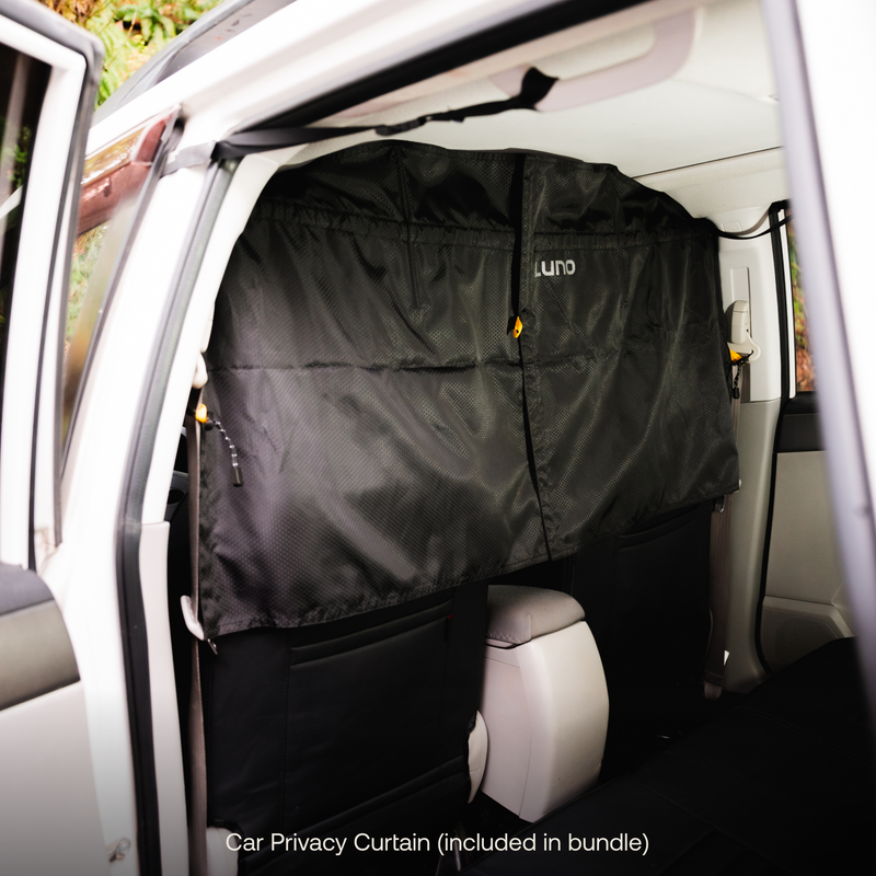 A black privacy curtain is installed inside a white car, separating the front seats from the back area. The curtain, labeled with the brand's name "Luno®," features a zippered closure in the center. Text at the bottom reads "Car Privacy Curtain (included in Car Camping Privacy Bundle)"—a perfect addition to your car camping essentials.