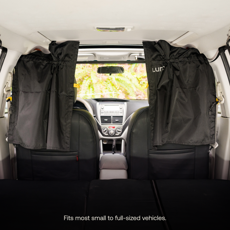 Interior view of a vehicle showcasing Luno® Car Privacy Curtains providing sun-blocking protection on the rear side windows. The picture, taken from the back seat facing forward, offers an unobstructed view of the dashboard and front seats. Text at the bottom reads, "Fits most small to full-sized vehicles.