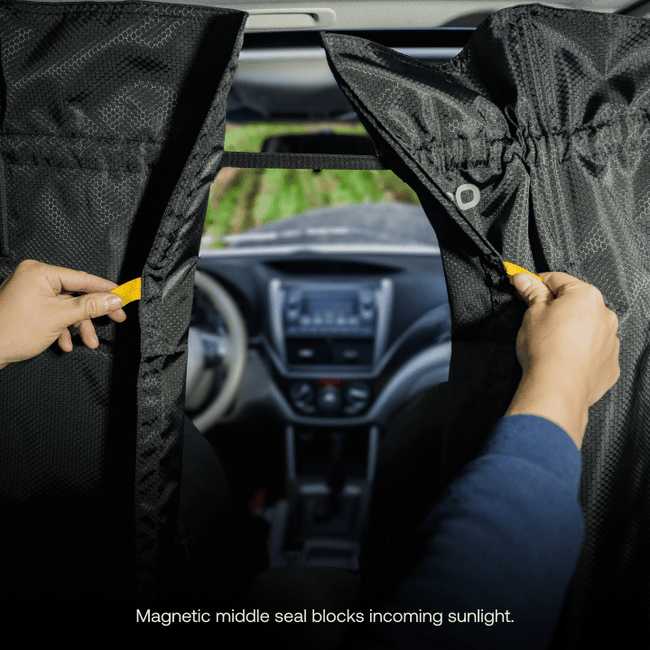 A person is holding two car window curtains from Luno HQ, slightly parted to reveal a view of the car's dashboard and windshield. Text at the bottom reads: "Magnetic middle seal blocks incoming sunlight, ideal for those in need of a Car Privacy Curtain solution.